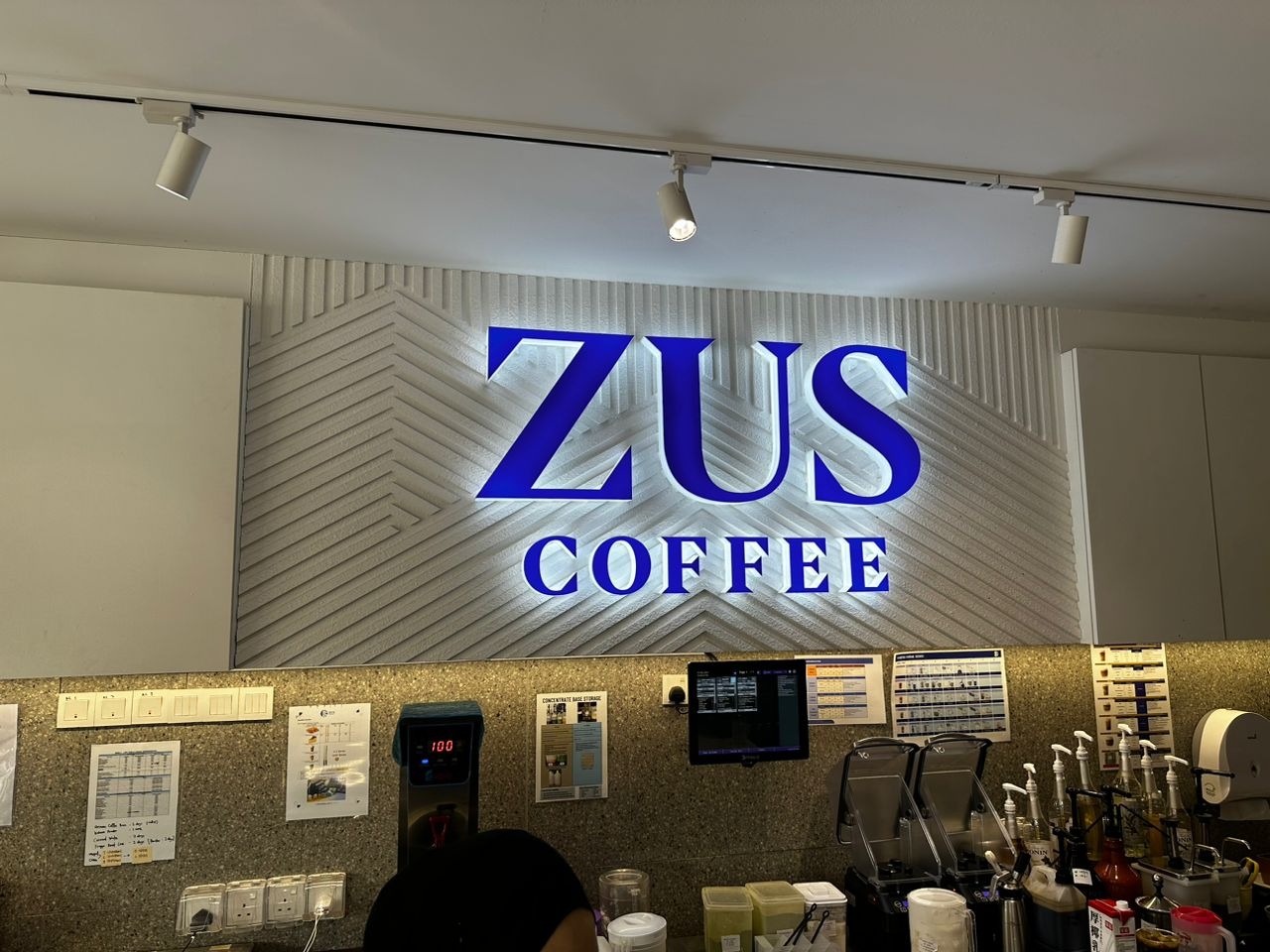 Completed coffee outlet service counter beneath an illuminated brand wall